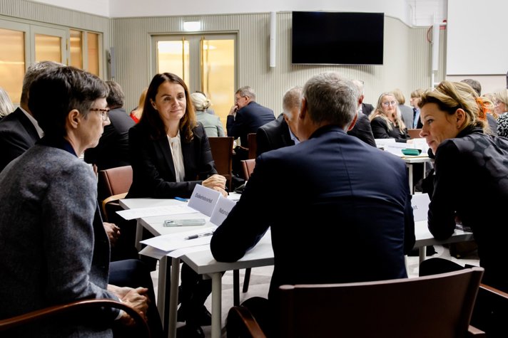 A number of persons are sitting around a table discussing.
