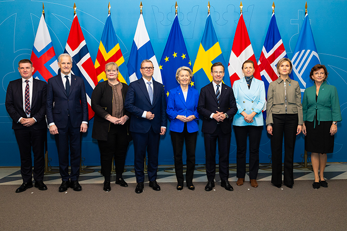 Aksel V. Johannesen, Mette Fredriksen, Ursula von der Leyen, Petteri Orpo, Ulf Kristersson, Katrin Sjögren, Jonas Gahr Støre, Kristrún Frostadóttir and Karen Ellemann stand in a row indoors against a blue background. Behind them is a row of flags: Faroe Islands, Denmark, EU, Finland, Sweden, Åland, Norway Iceland, Nordic Council.