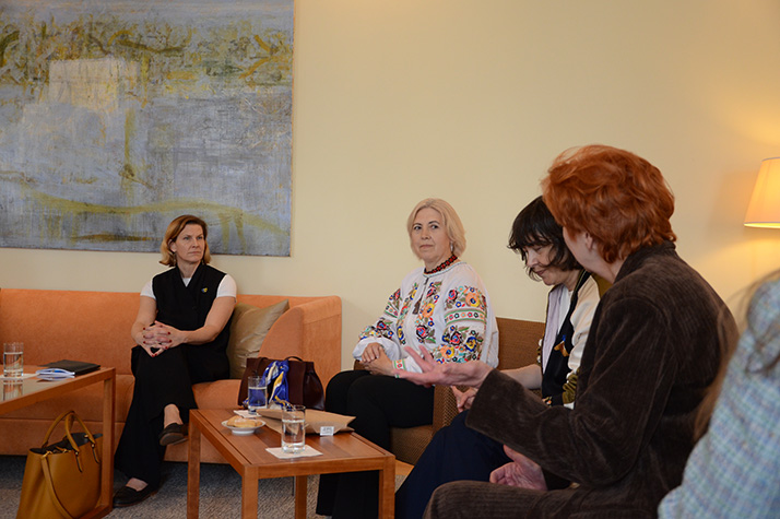 Minister for Gender Equality Nina Larsson sits with several people in a meeting room during a visit to the organization SEMA, with chairs, a small table with glasses of water, and a painting on the wall in the background.