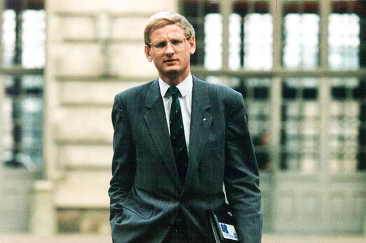 Carl Bildt with a briefcase under his arm outdoors in front of a building.