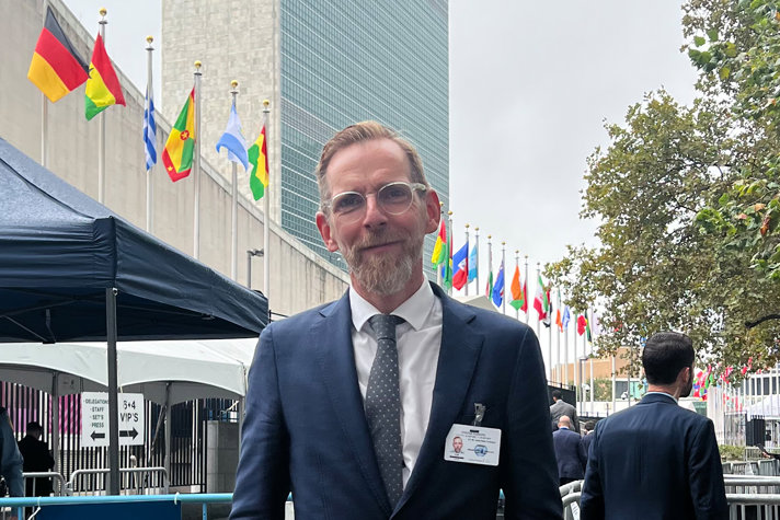 Minister for Health and Social Affairs Jakob Forssmed standing in front of UN Headquarters in New York. A skyscraper and a row of flags can be seen behind him.
