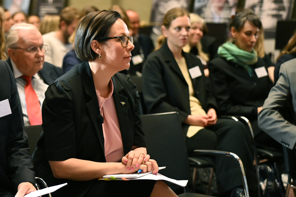 Minister for Foreign Affairs Maria Malmer Stenergard among a crowd of people, listening to someone speaking on stage. 