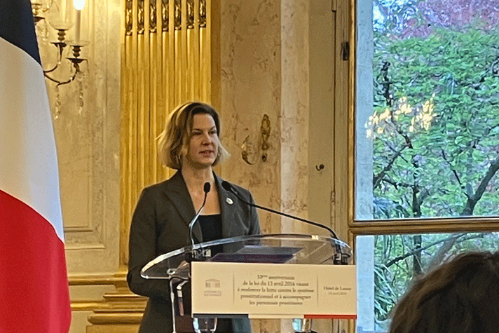 Nina Larsson, the Swedish Minister for Gender Equality makes a speech. The French flag is to her left and a window on her right.