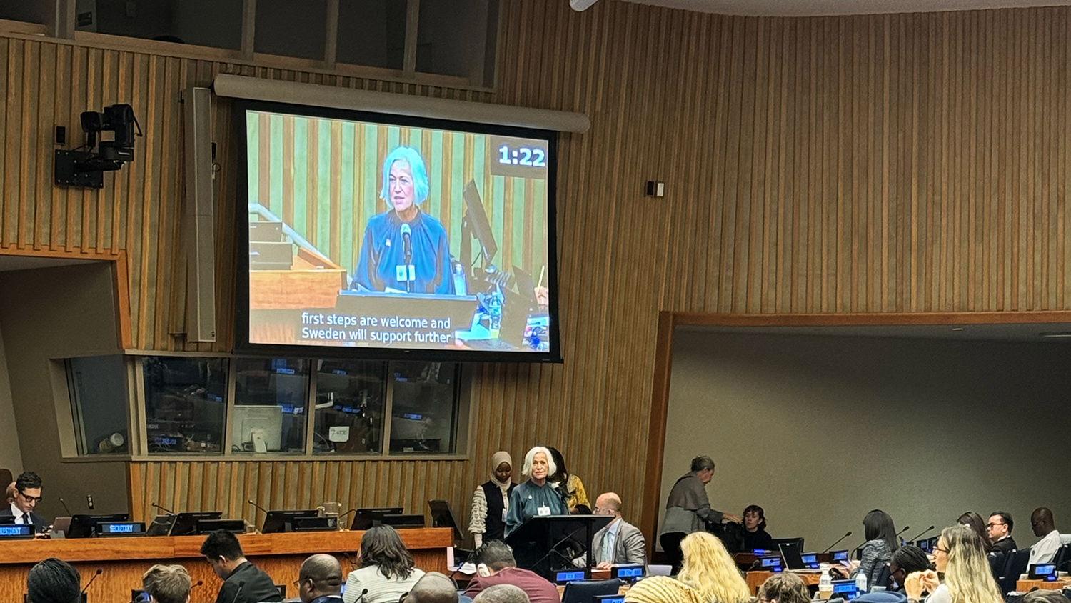 Minister Ankarberg Johansson delivers a speech. Her face is on a big screen in an auditorium.