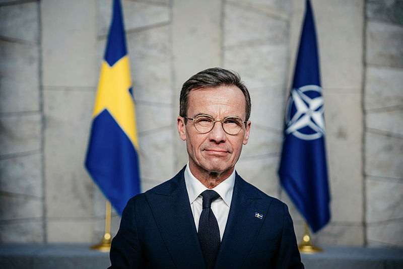  Kristersson standing in front of the Swedisf flag and the NATO flag.