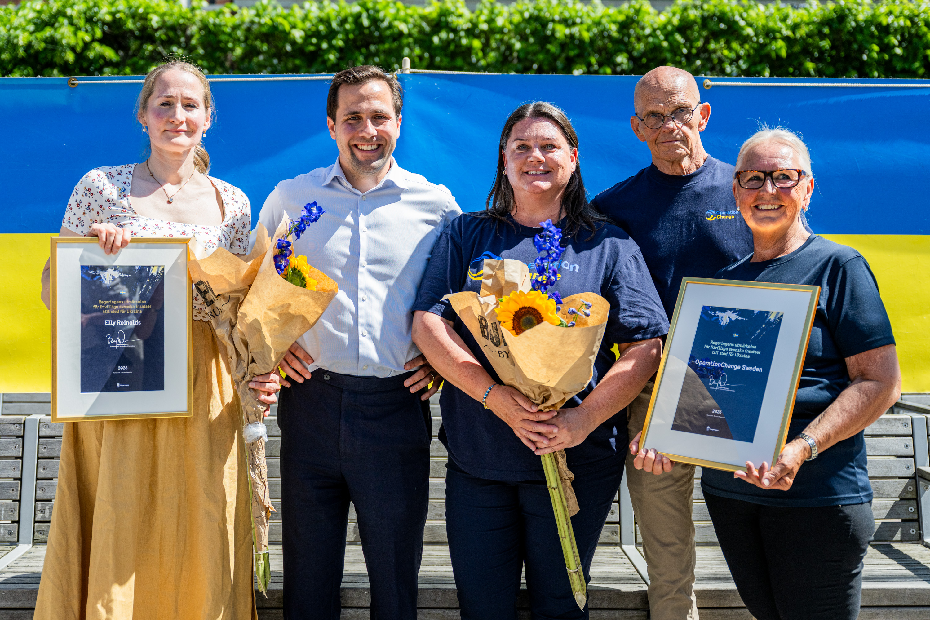 Benjamin Dousa togheter with Elly Reinolds and representatives from OperationChange. The recipients are holding flowers and diplomas.