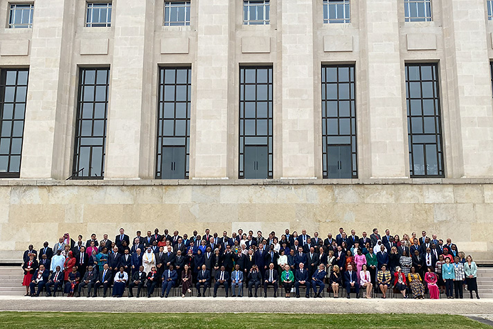 About one hundred men and women gathered on stairs in front of monumental building.