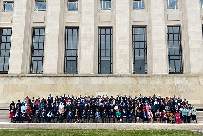 About one hundred men and women gathered on stairs in front of monumental building.